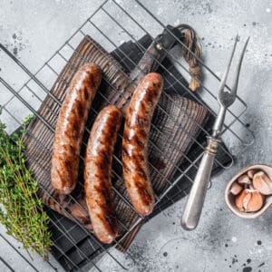 Grilled beef and lamb meat sausages with rosemary herbs on grill. Gray background. Top view.